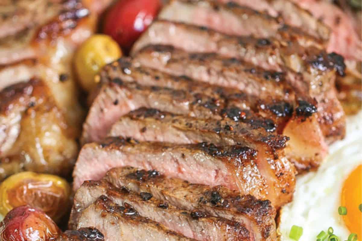 Sliced grilled steak with a seared crust, served with roasted cherry tomatoes and a fried egg on the side—one of those delicious meals perfect for easy cleanup.