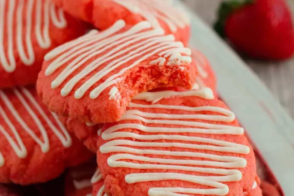 A stack of pink cookies with white icing drizzle, one cookie is bitten, and a strawberry peeks out in the background—perfect creative bake sale treats to wow your crowd.