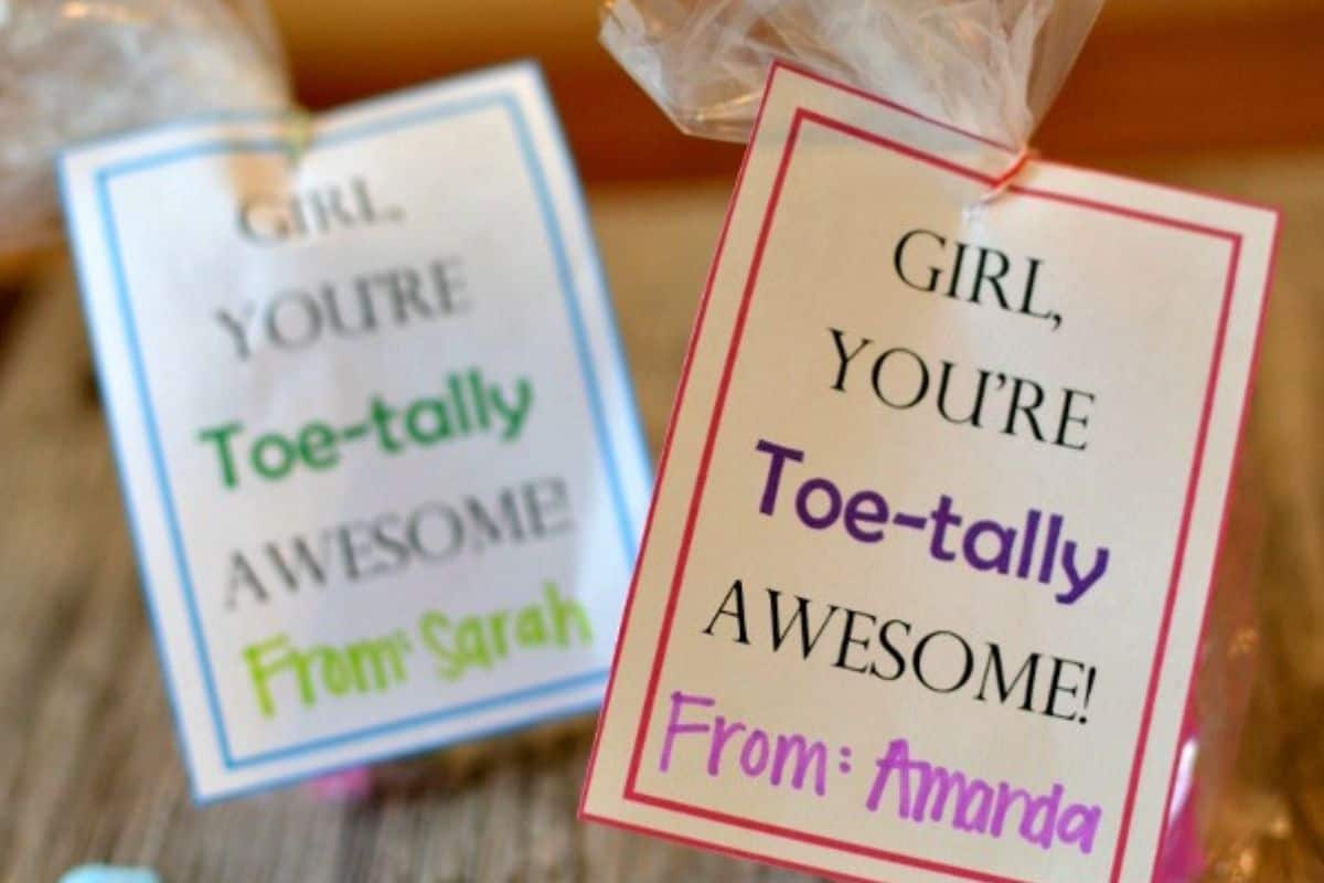 Two gift bags with tags that read "GIRL, YOU'RE Toe-tally AWESOME!" signed "From: Sarah" and "From: Amanda" make creative Valentines for kids—perfect as printable Valentines for classroom celebrations.