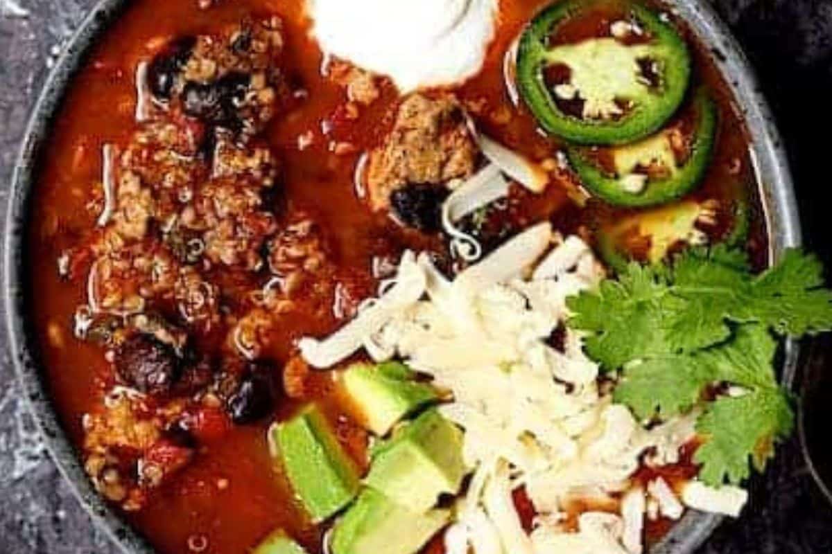 A bowl of chili topped with sliced jalapeños, shredded cheese, avocado chunks, sour cream, and fresh cilantro—one of those must-try chili recipes everyone loves.