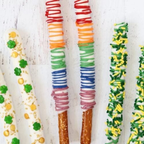 Assorted pretzel rods decorated with colorful icing and sprinkles, arranged on a white surface with green clover and gold coin decorations nearby—perfect for adding Irish Luck to your creative recipes.