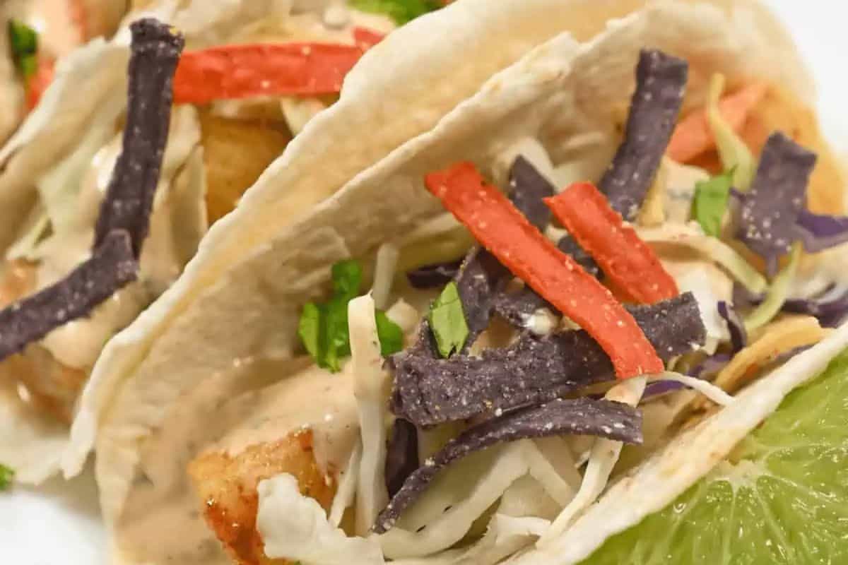 Two soft shell tacos filled with shredded cabbage, tortilla strips, sauce, and herbs, served next to a slice of lime—perfect for Lent or anyone seeking easy recipes for delicious fish dishes.