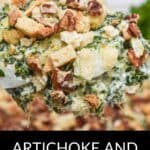 Close-up of a spoonful of Artichoke and Spinach Dip Recipe topped with croutons and chopped pecans, with the creamy dip visible in the background.