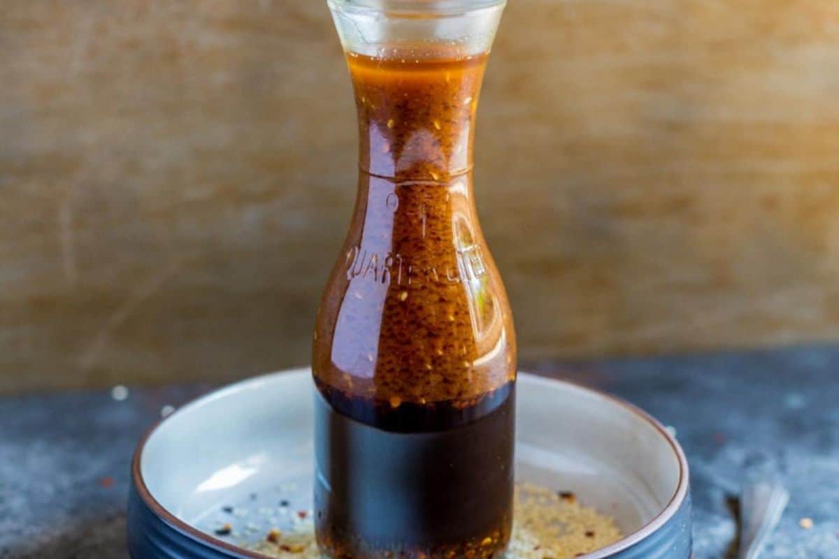 Asian salad dressing in a glass bottle, showing its dark color and visible herbs and spices.