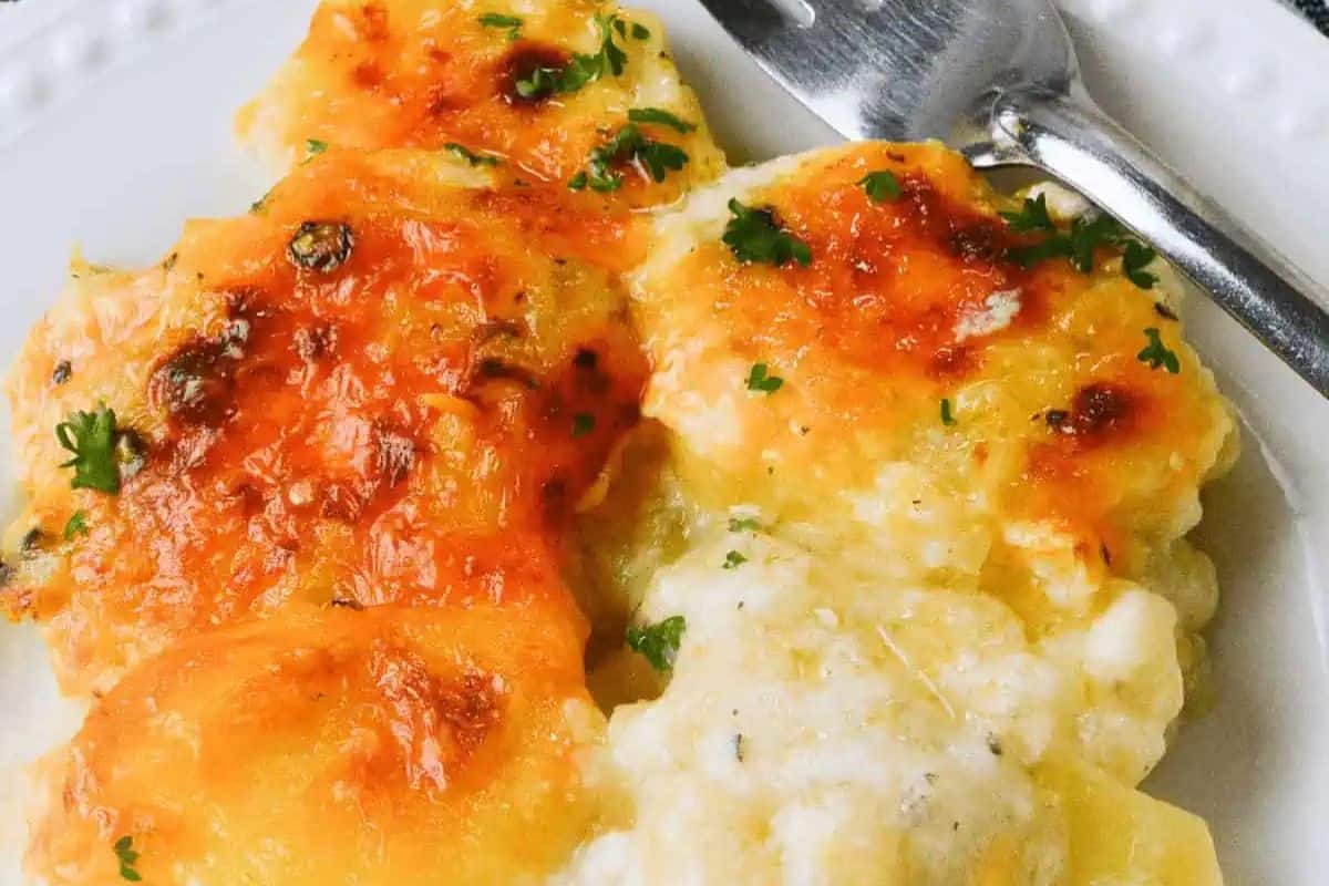 A plate of golden, bubbly au gratin potatoes topped with melted cheese and garnished with parsley. Perfect for those seeking delicious recipes, a fork rests beside the serving, inviting you to dive in.