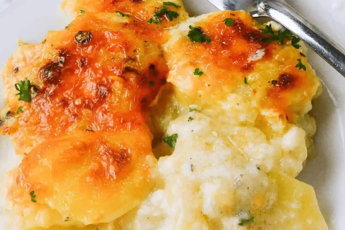 Close-up of cheesy au gratin potatoes with a golden-brown crust, garnished with parsley. A fork rests on the plate—an irresistible addition to your Easter side dishes that's perfect for elevating holiday meals.