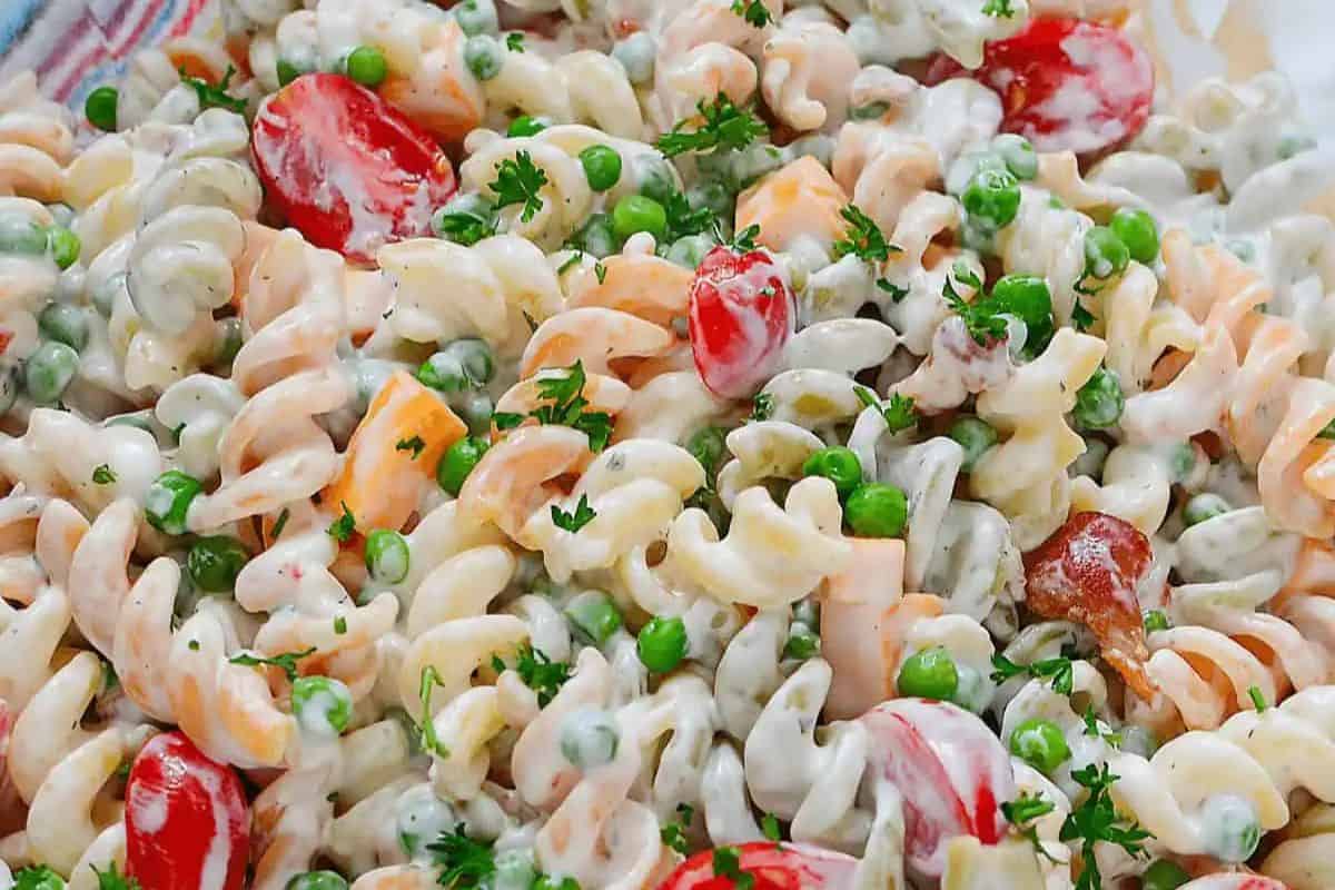 A delightful spring salad recipe featuring a bowl of pasta salad with rotini, cherry tomatoes, peas, bacon, and a creamy dressing, all elegantly garnished with parsley.