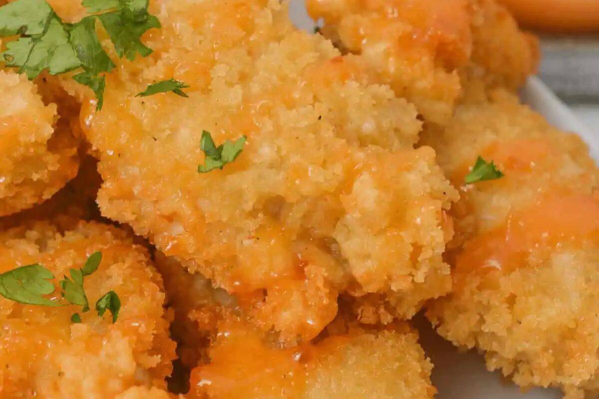 Close-up of crispy breaded chicken tenders topped with a drizzle of orange sauce, garnished with fresh parsley—an adorable addition to any baby shower menu.