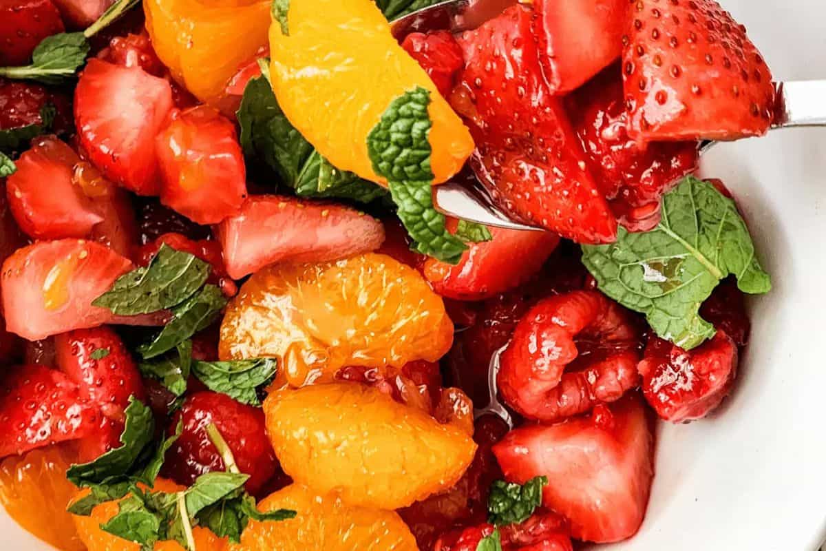 A fresh delight perfect for spring brunch recipes, this close-up features a fruit salad with sliced strawberries, orange segments, raspberries, and mint leaves artfully arranged in a white bowl.