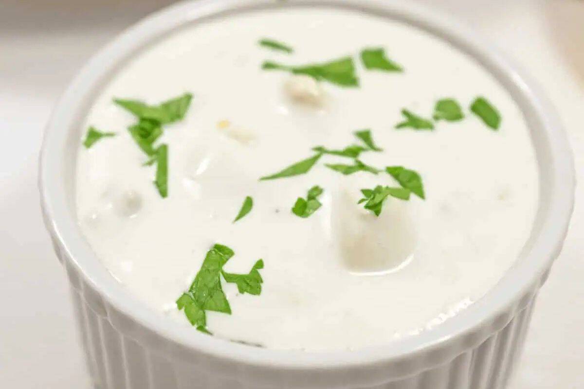 Blue cheese dressing in a white ramekin, showing the creamy white texture, chunks of blue cheese, and green herbs.