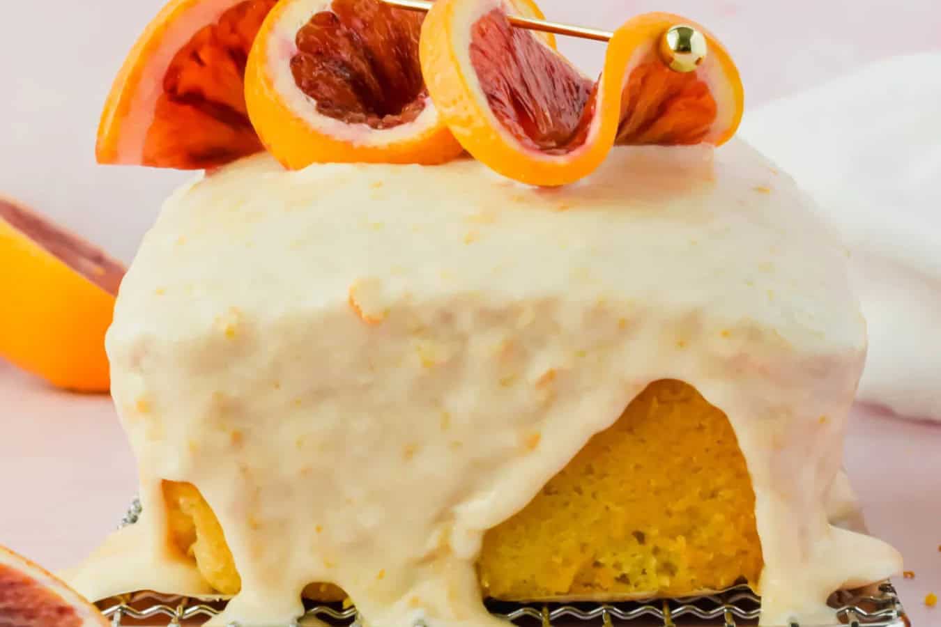 A square citrus cake, one of the most beautiful spring desserts, is topped with drippy white icing and garnished with blood orange slices on a skewer.