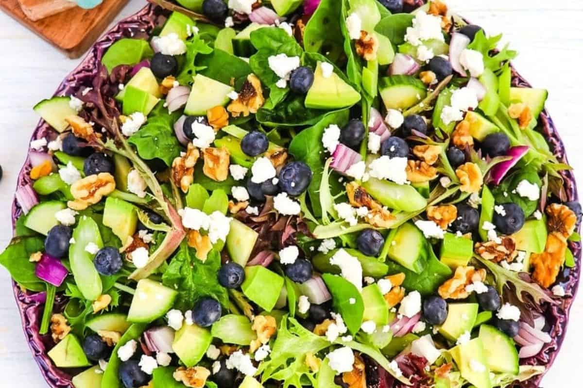 A plate of the best Spring Salad with mixed greens, blueberries, cucumber, walnuts, feta cheese, and red onion.