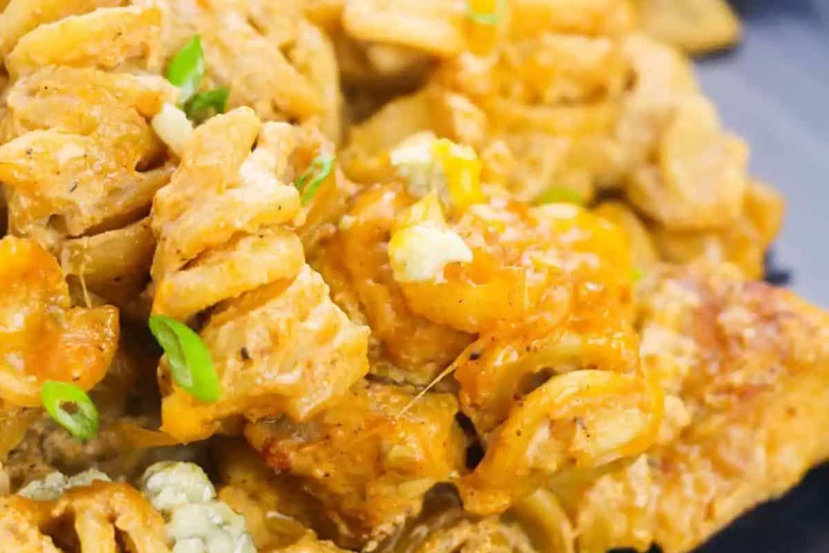 Close-up of a must-try rotini pasta dish in a creamy, cheesy sauce, topped with spring-fresh green onion slices and crumbled cheese.