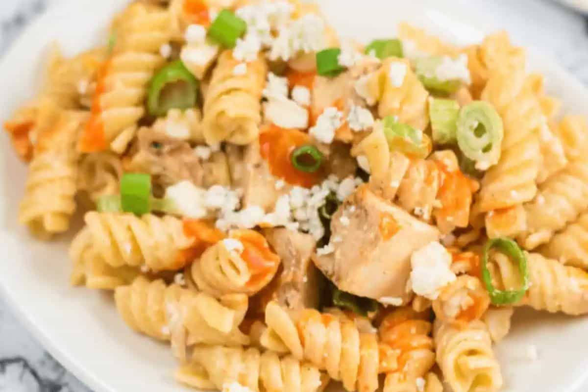 A plate of rotini pasta mixed with chunks of chicken, sliced green onions, crumbled cheese, and small pieces of red pepper is perfect for the best spring salad season.