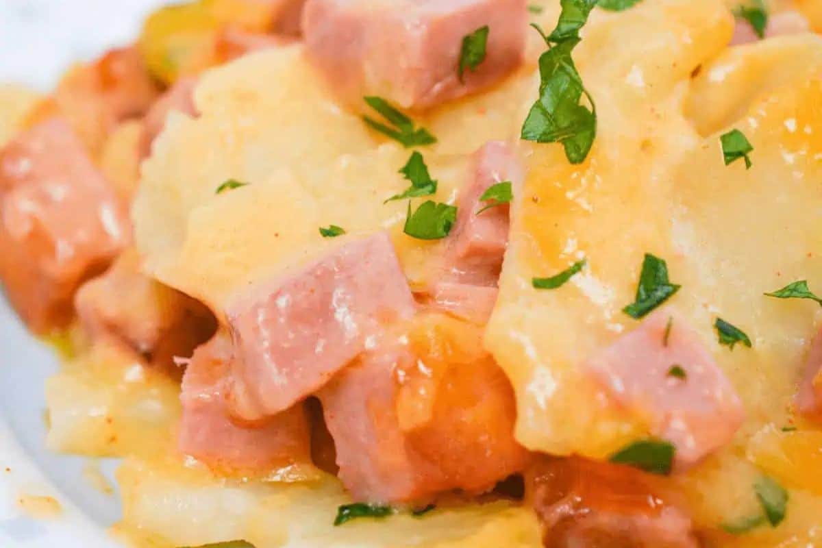 A close-up of a spring brunch casserole featuring chunks of ham, melted cheese, and potatoes, all garnished with chopped parsley.