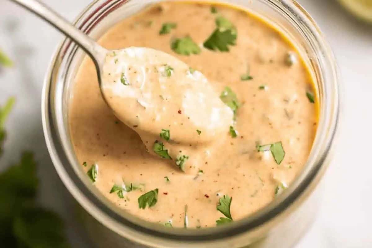 Chipotle ranch dressing in a glass jar, with a spoon scooping out a portion, showing its creamy texture and visible herbs.