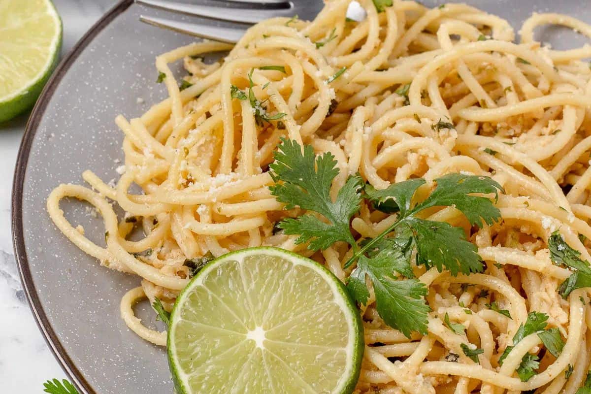 A masterful plate of spaghetti garnished with cilantro and a lime slice, perfect for beginners exploring pasta dishes. Served on a gray plate with a fork, it's an inviting meal.