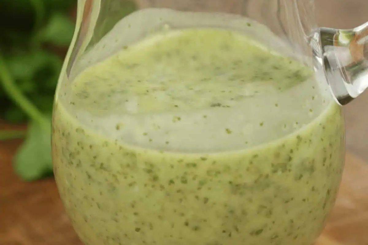 Cilantro lime vinaigrette in a clear glass pitcher, showing the light green color and visible herbs.