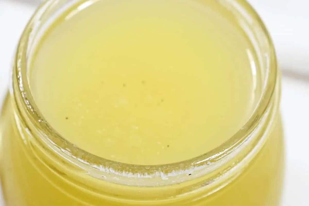 Pale yellow citrus vinaigrette in a clear glass jar, viewed from directly above.