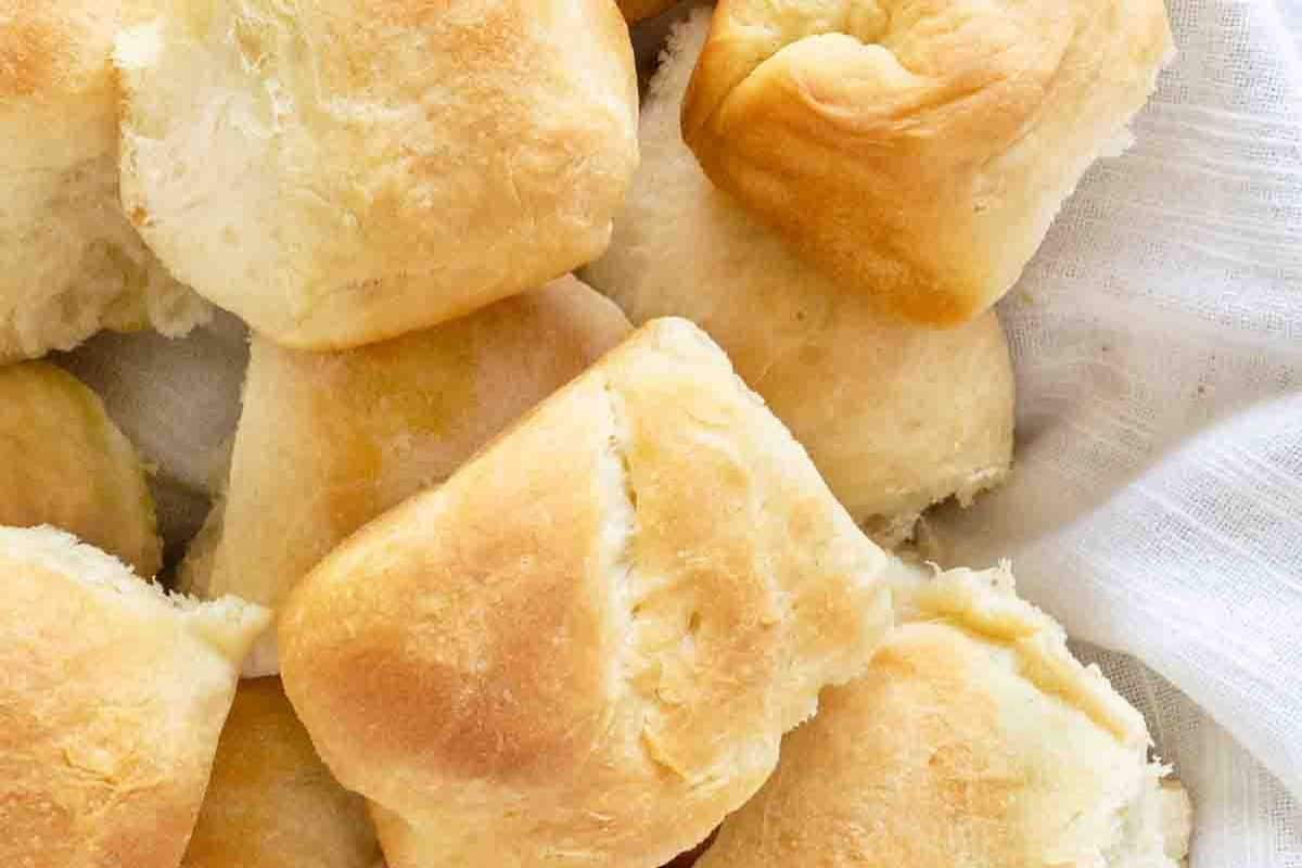 A close-up of several golden brown dinner rolls, perfect as side dishes for Easter, stacked together on a white cloth.