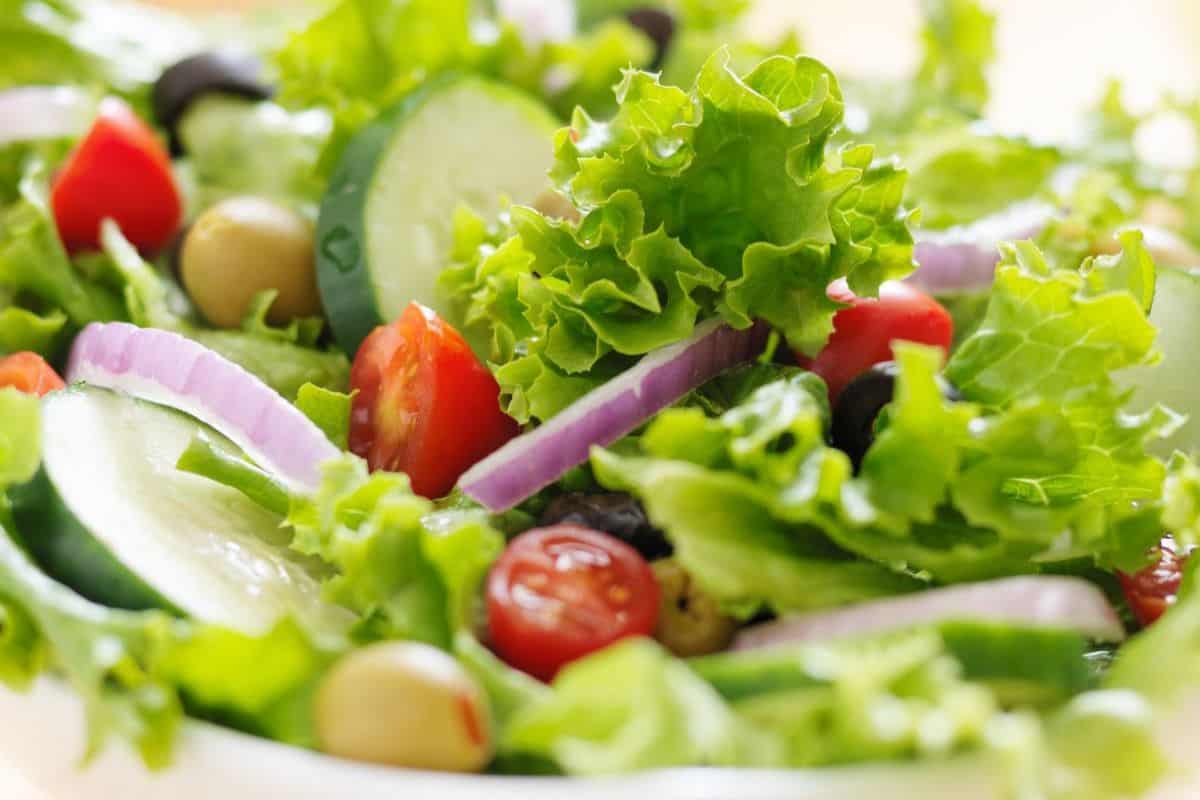 A bowl of salad with mixed greens, cherry tomatoes, cucumbers, red onion, olives and Panera Green Goddess dressing.