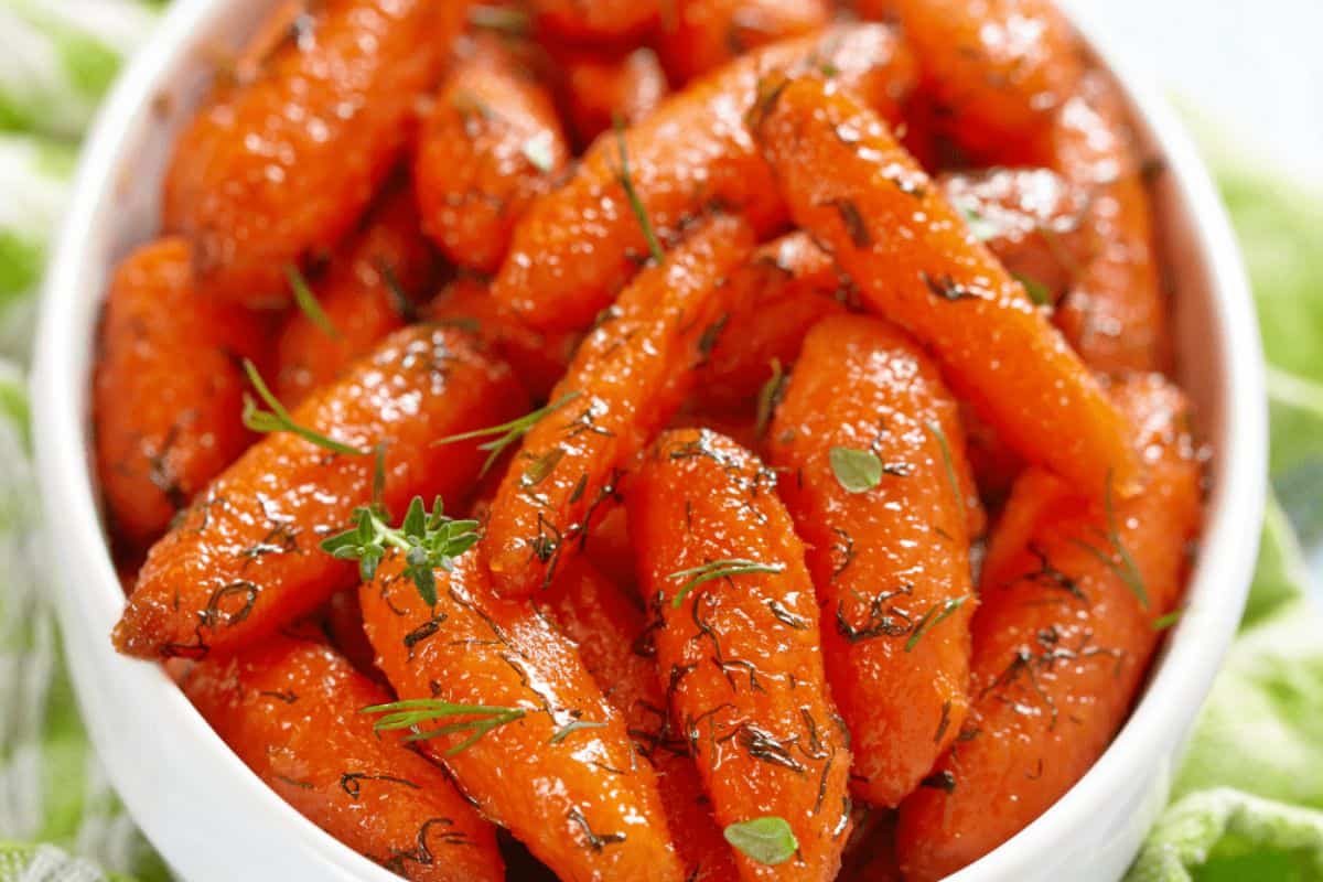 A bowl of glazed baby carrots garnished with herbs, perfect for Easter side dishes.