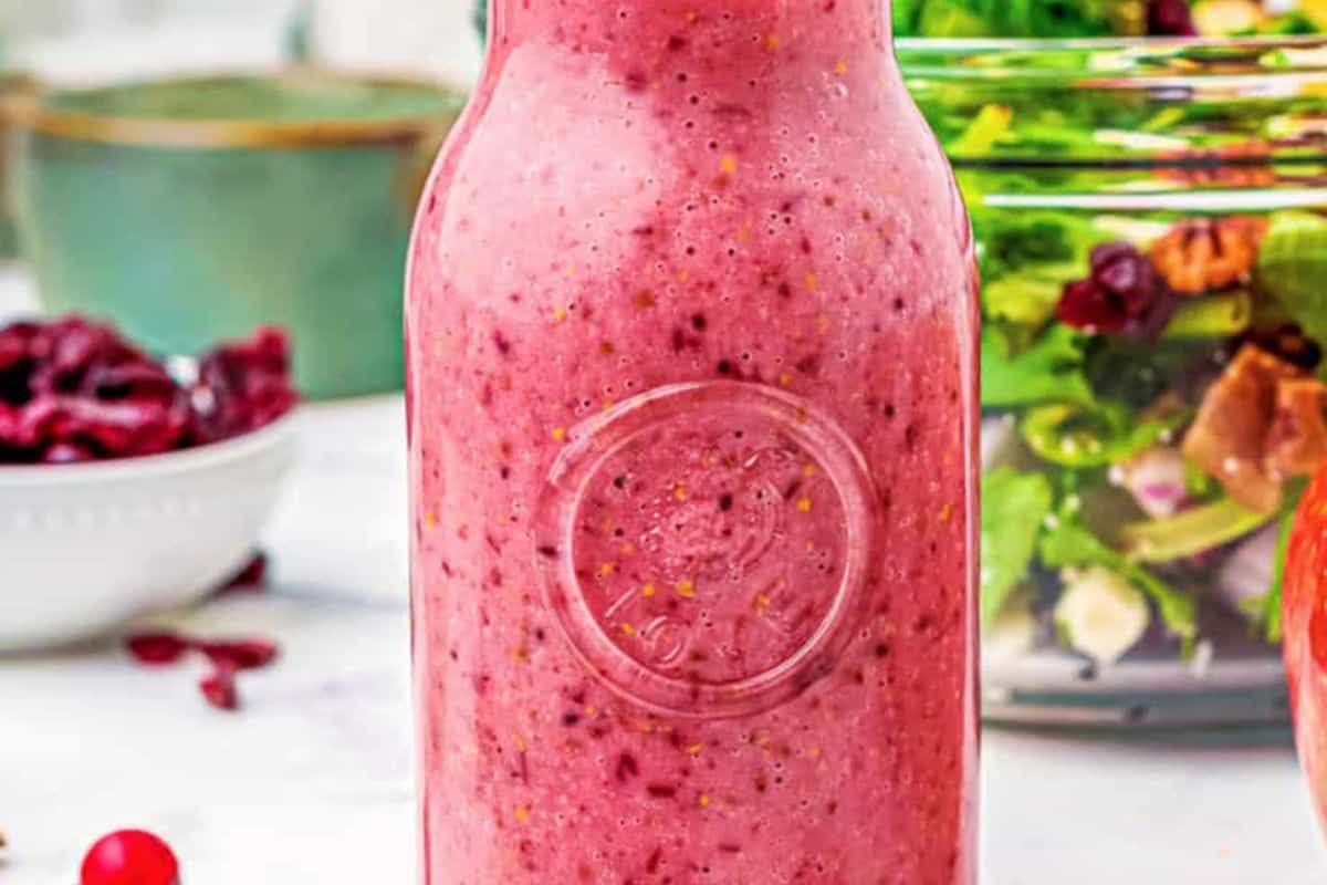 Pink-red cranberry vinaigrette salad dressing in a clear glass bottle, showing its vibrant color and visible cranberries.