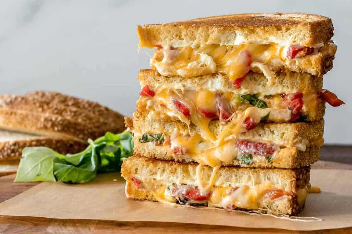 Cream cheese grilled cheese sandwich with melted cheese, red peppers, and basil, stacked on toasted bread.