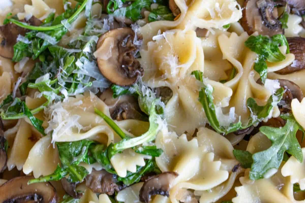 Close-up of a must-try spring pasta dish featuring bow tie noodles, mushrooms, arugula, and grated cheese.