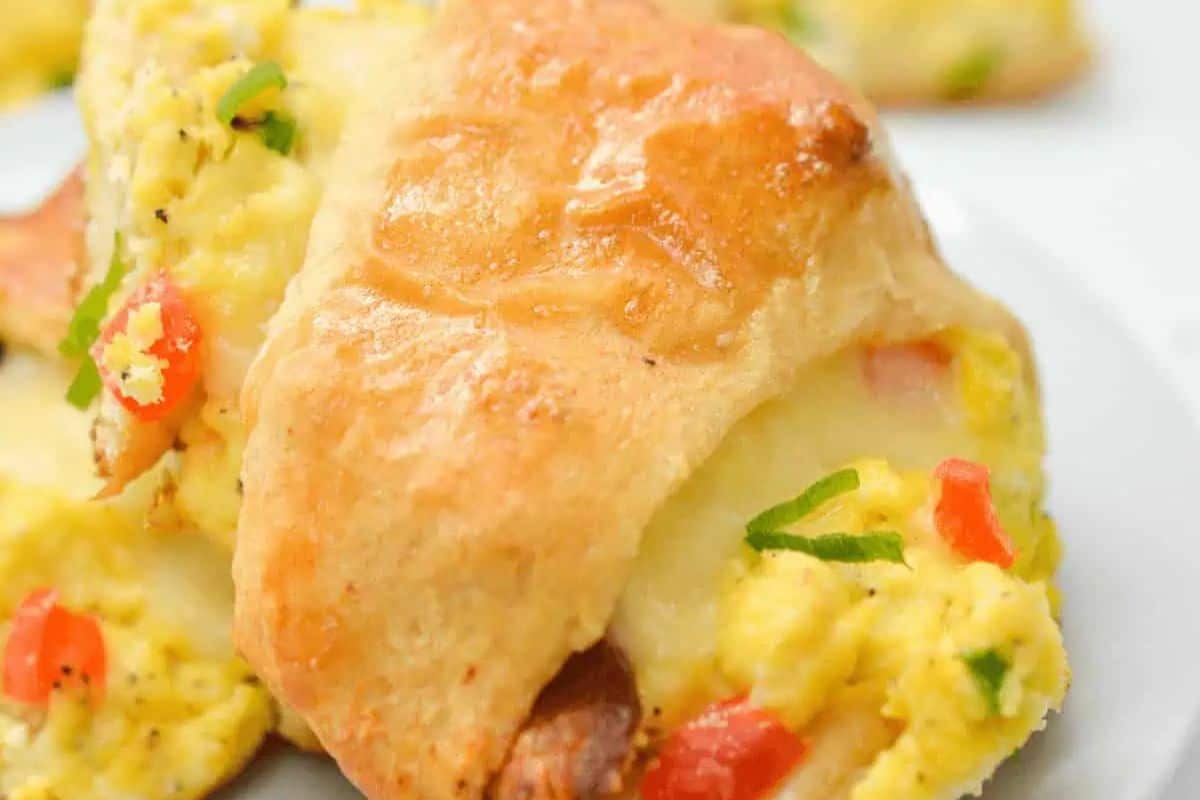 Close-up of a croissant sandwich filled with scrambled eggs, cheese, and diced red peppers on a white plate—perfect for your Easter brunch spread.