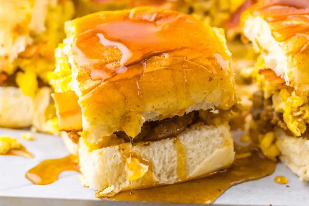 Close-up of a breakfast slider with sausage, egg, and cheese, drizzled with maple syrup on a soft bun—an irresistible addition to your Easter brunch recipes.
