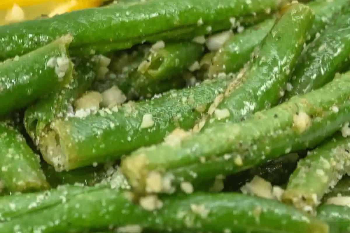 Close-up of cooked green beans sprinkled with grated cheese and small garlic pieces, making it a delightful addition to your Easter side dishes.