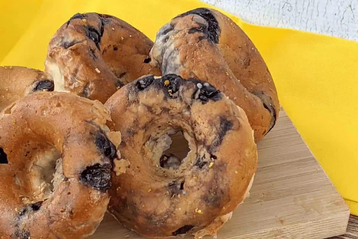 Five blueberry donuts rest invitingly on a wooden cutting board against a vibrant yellow cloth background, perfect for those seeking fresh ideas for spring brunch recipes.