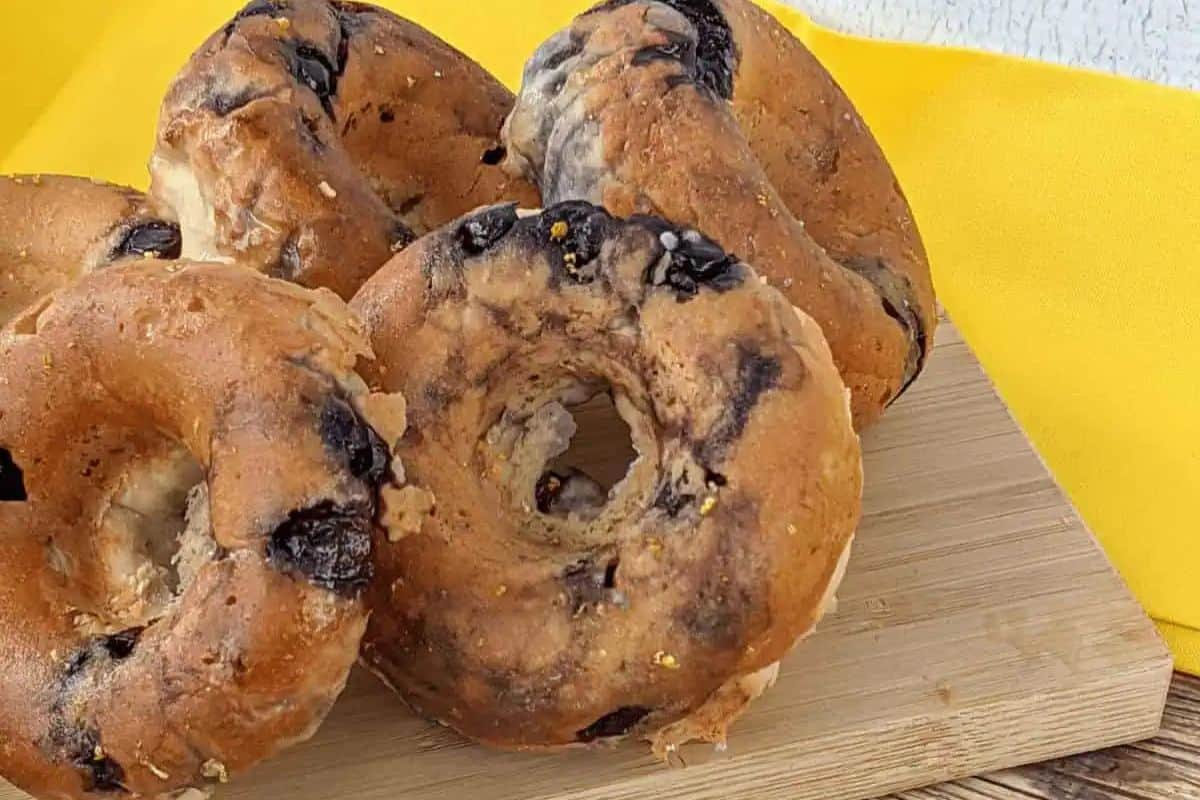 Five blueberry donuts rest on a wooden board with a yellow cloth in the background, offering a perfect addition to your Easter brunch recipes.