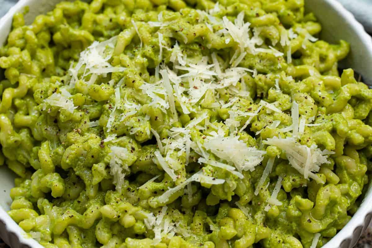A classic spring dish: a bowl of green pea pasta luxuriously coated in vibrant green pesto, topped with freshly grated parmesan cheese and a sprinkle of black pepper.