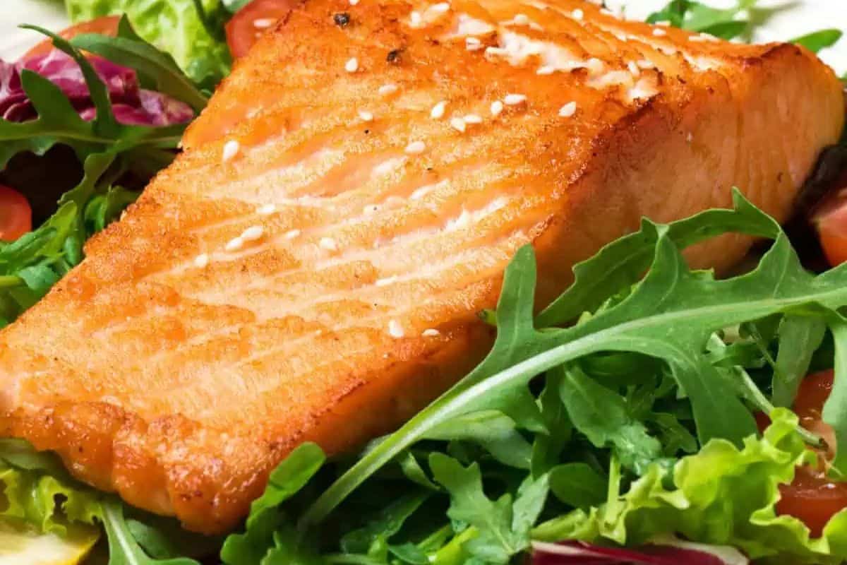 Grilled salmon fillet atop a vibrant spring salad of mixed greens and cherry tomatoes, elegantly garnished with sesame seeds.