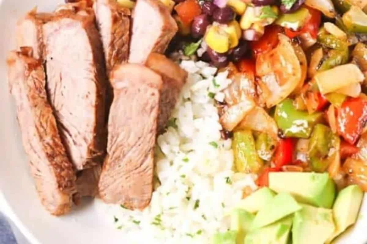 Savor the flavors of a homemade burrito bowl featuring sliced steak, rice, and avocado alongside sautéed peppers, onions, black beans, and corn. Perfect for a vibrant Cinco de Mayo celebration on your plate.
