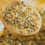A wooden spoon holds a coarse homemade spice blend. Text on image reads: “26 Homemade Spice Blends Everyone Needs.”.