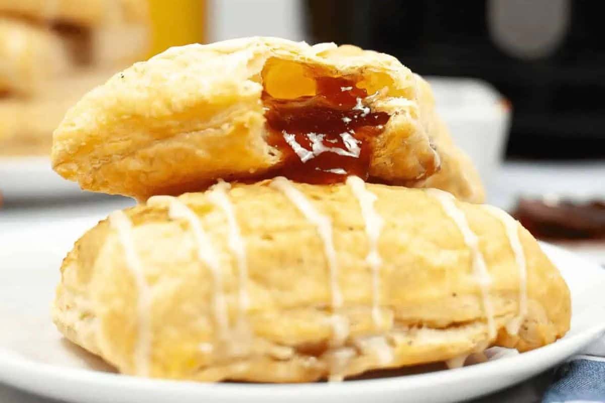 A close-up of two glazed pastry turnovers on an elegant plate. Perfect for spring brunch recipes, the top pastry is impressively broken open, revealing a golden jam filling that promises a delightful treat.