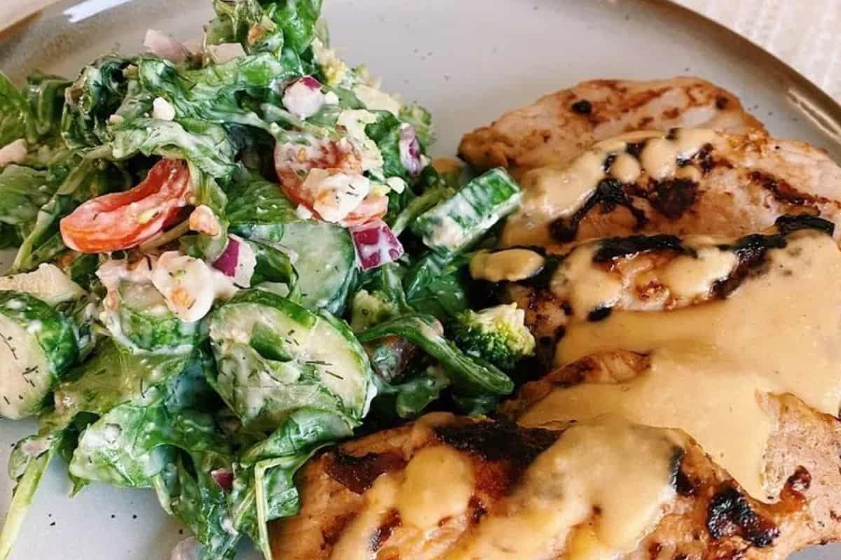 Salad with mixed greens and grilled chicken topped with a sauce, featuring a hummus-based dressing.