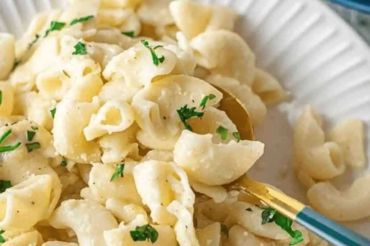 A plate of pasta shells with a creamy sauce, garnished with chopped herbs, and served with a gold-colored utensil makes for an exquisite Easter side dish.