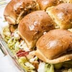 A tray of Italian sliders features baked sandwich sliders, stacked with layers of lettuce, savory meats, and pickles on soft, glazed buns.