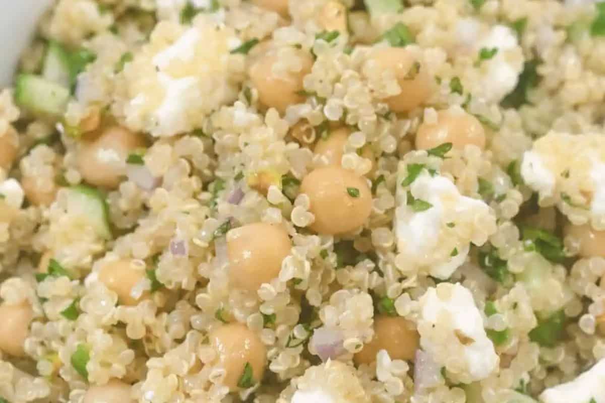 A close-up of a quinoa salad featuring chickpeas, crumbled feta cheese, and chopped herbs, offering a fresh and textured mixture. Try this season's best spring salad for a delightful culinary experience!.