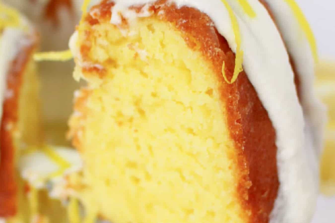 A close-up of a sliced lemon bundt cake, crowned with white icing and vibrant lemon zest, embodies the essence of beautiful spring desserts.