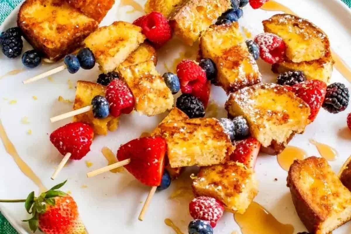 Perfect for spring brunch recipes, this delightful dish features French toast and berry skewers elegantly arranged with strawberries, blueberries, raspberries, and blackberries—all drizzled with syrup on a pristine white plate.