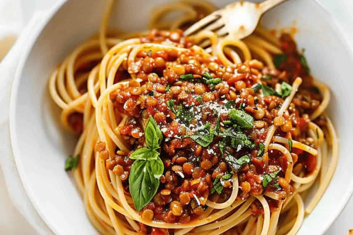 A masterful bowl of spaghetti topped with lentil tomato sauce, garnished with fresh basil leaves and grated cheese, perfect for beginners looking to explore delightful pasta dishes, with a fork beside it.