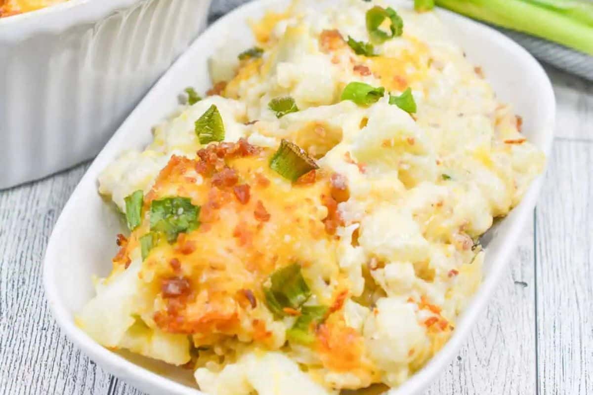 A delightful Easter side dish, this loaded cheesy cauliflower casserole is topped with melted cheese, bacon bits, and green onions. Perfectly presented in a white bowl on a rustic wooden table, it's sure to be a holiday favorite.