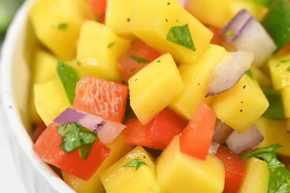 A close-up of a vibrant mango salsa featuring diced mango, red bell peppers, red onions, and cilantro in a white bowl—a perfect dip for your Cinco de Mayo party.