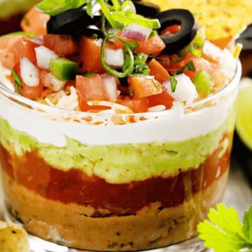 A flavor-packed dip perfect for a Cinco de Mayo party, this layered delight features refried beans, guacamole, sour cream, salsa, shredded cheese, diced tomatoes, green onions, and black olives—all ready to scoop up with crunchy tortilla chips. Lime and cilantro add the final festive touch.