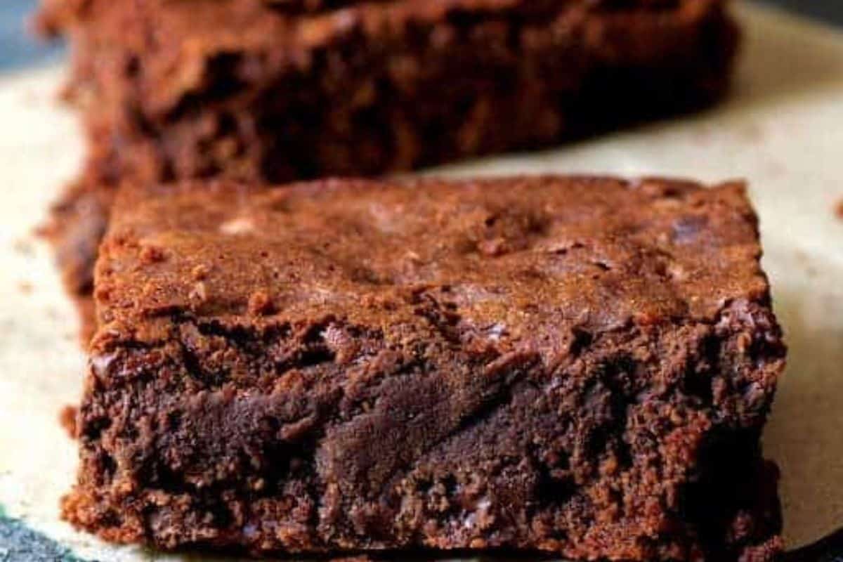 A close-up of a chocolate brownie on a parchment paper background. The dessert has a rich, dark chocolate texture with a slightly crumbly surface, perfect for any Cinco de Mayo celebration.
